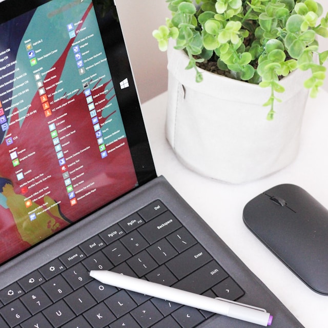 partial laptop screen with pen, mouse, and plant